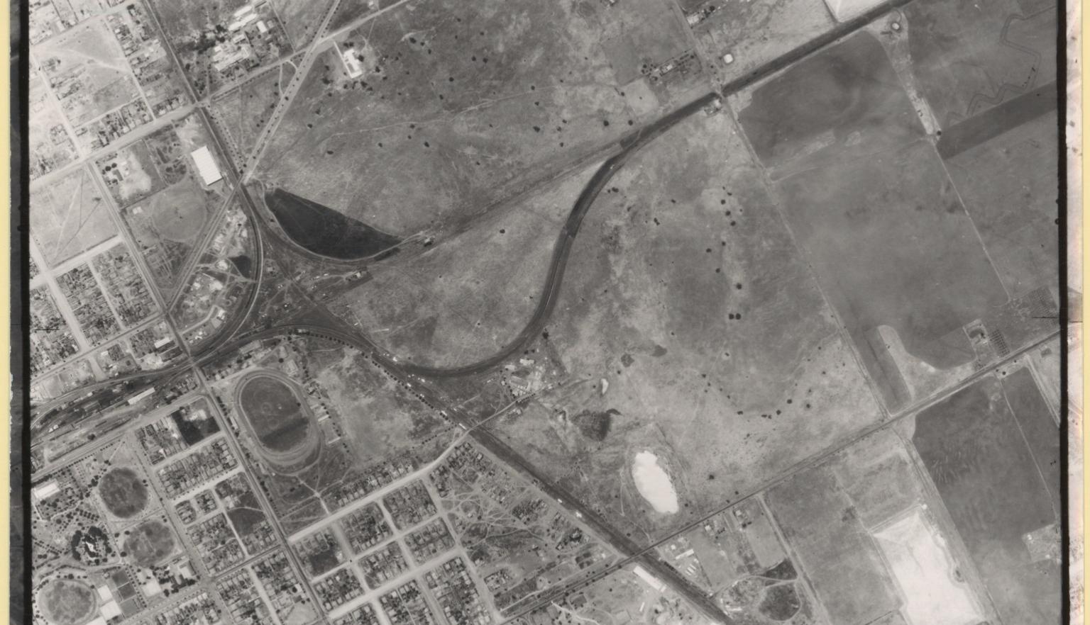 A black and white aerial image of Dubbo. On the left of the image is houses and the community, and on the right are open space and parcelled land.  